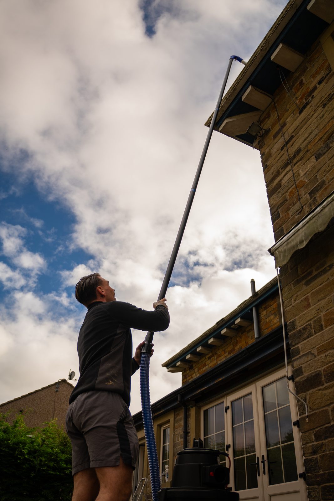 Vacuum pole clearing a gutter on a stone house