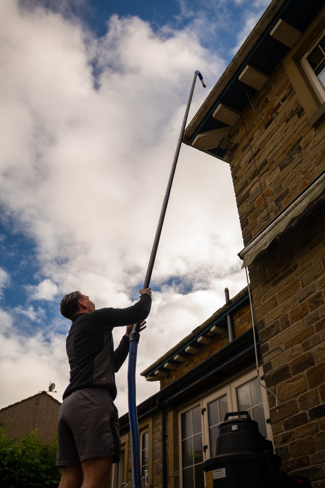 George clearing a first-floor gutter with a vacuum pole from the ground